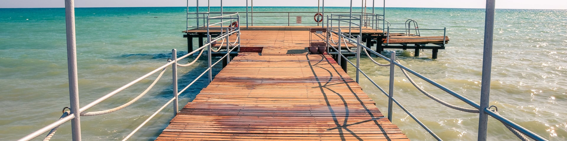 A wooden pier extending into a calm sea with clear skies.
