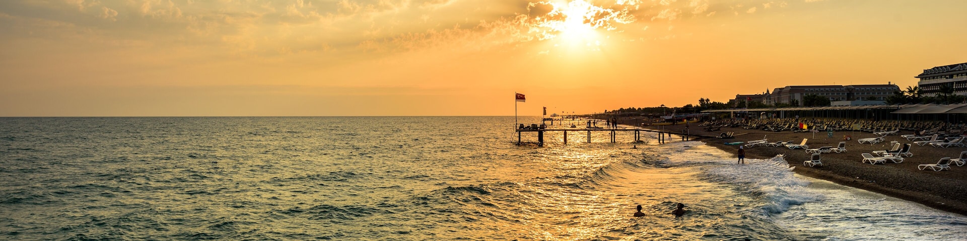 Un atardecer sobre el océano con un muelle y sillas de playa.