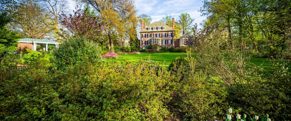 A large brick house with a green roof, surrounded by lush gardens and trees.