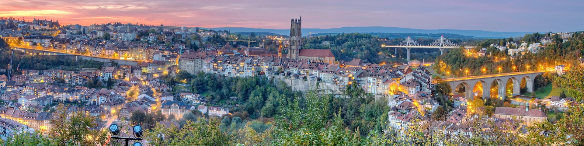 Vista panorâmica de uma cidade com uma igreja imponente, uma ponte e um rio.