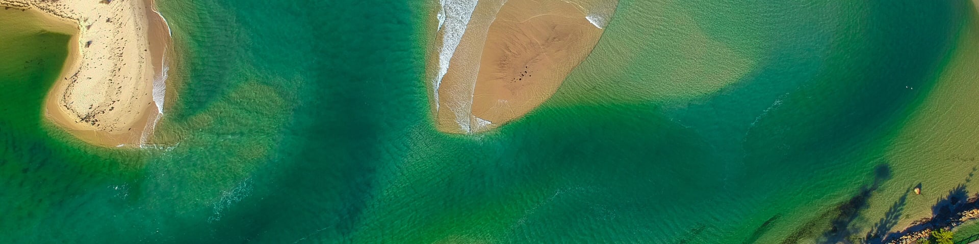 An aerial view of a coastal area with clear green waters, sandy beaches, and a distinct green lagoon.