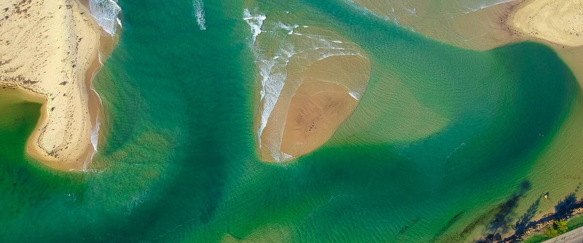 An aerial view of a coastal area with clear green waters, sandy beaches, and a distinct green lagoon.
