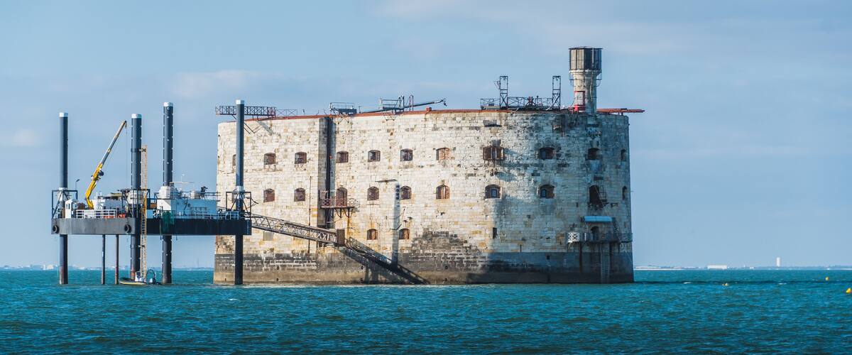 A large, isolated concrete structure with a staircase leading up to a platform, surrounded by water.