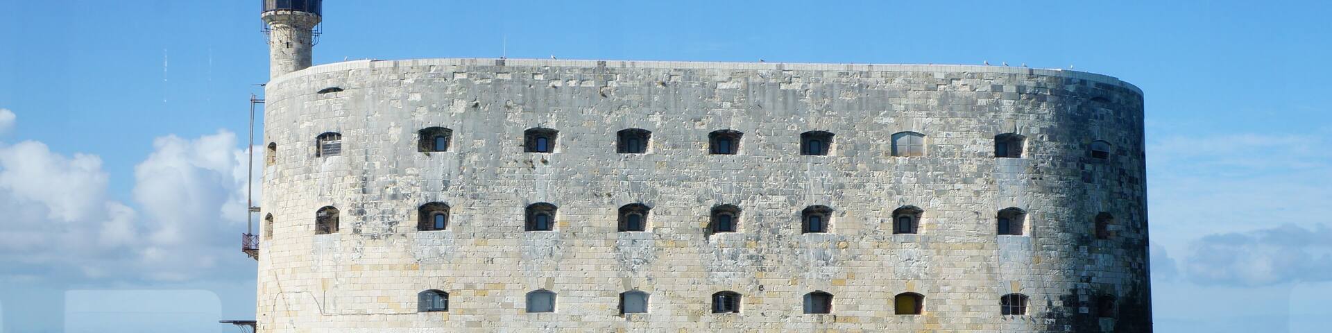 A large, cylindrical stone structure with multiple small windows, floating in calm water under a clear sky.