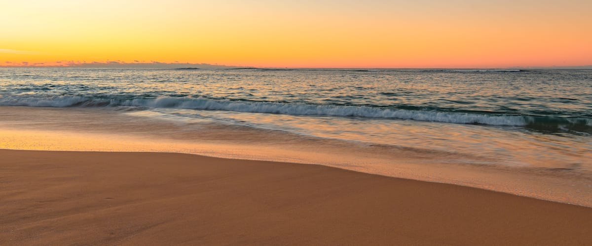 A beach at sunset with waves gently lapping the shore.