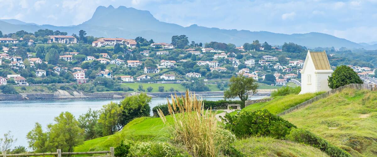A coastal town with houses on a hillside, a lighthouse, and mountains in the background.