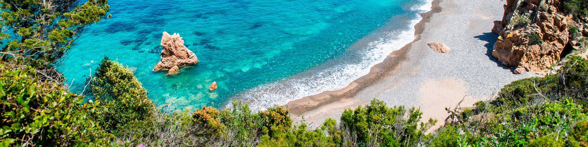 A coastal landscape with clear turquoise waters, rocky outcrops, and a sandy beach.