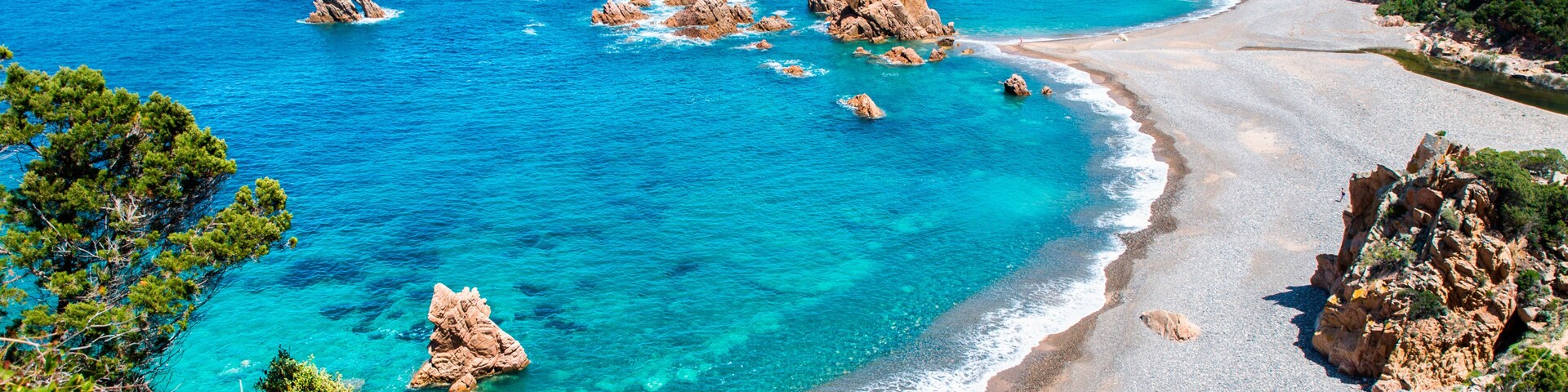 A coastal landscape with clear turquoise waters, rocky outcrops, and a sandy beach.