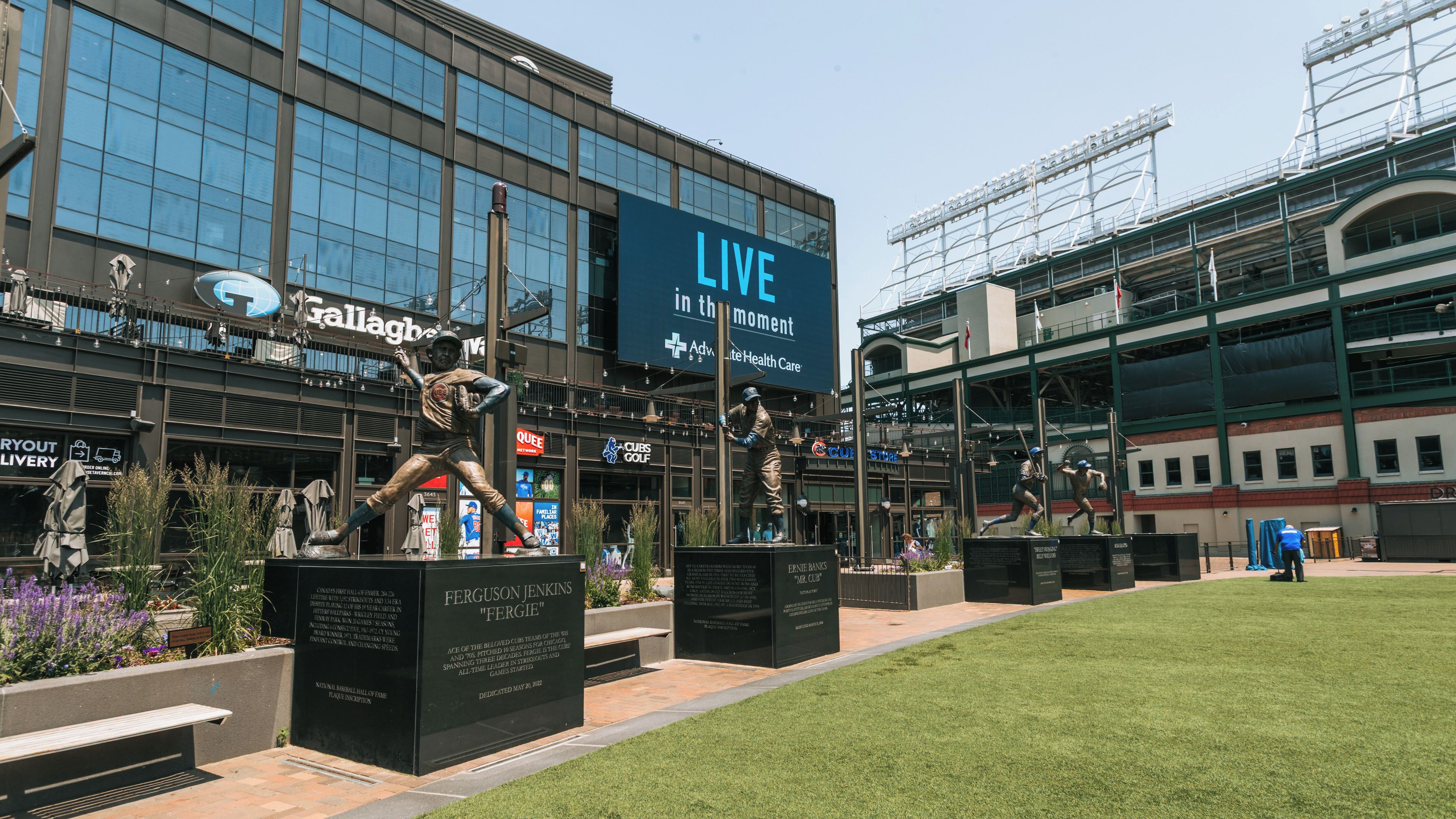 A baseball stadium with a large 'LIVE in the moment' sign, a statue of a baseball player, and a plaque dedicated to Ferguson Jenkins.