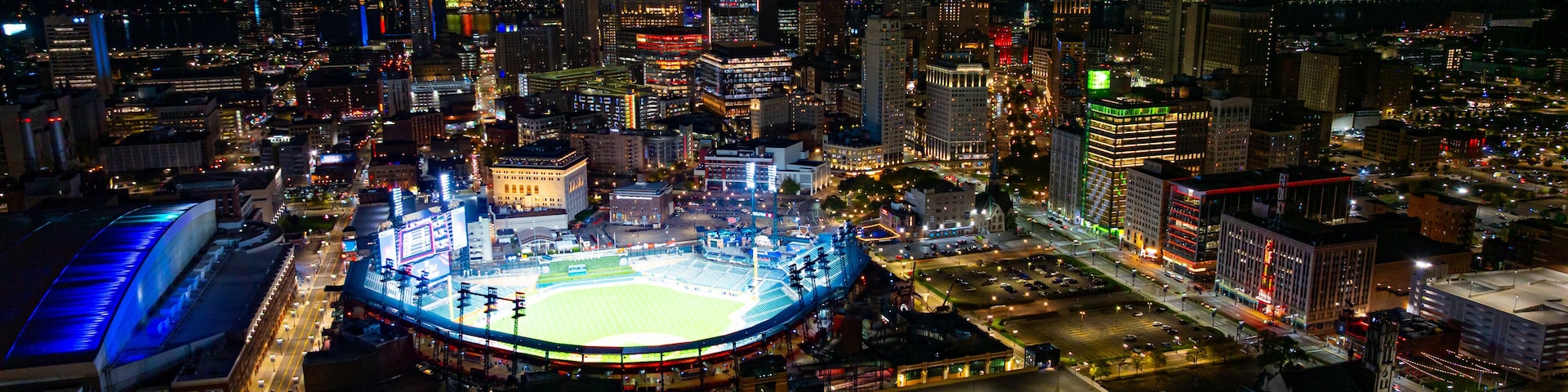Vista noturna de um estádio grande, rodeado por edifícios e ruas da cidade.