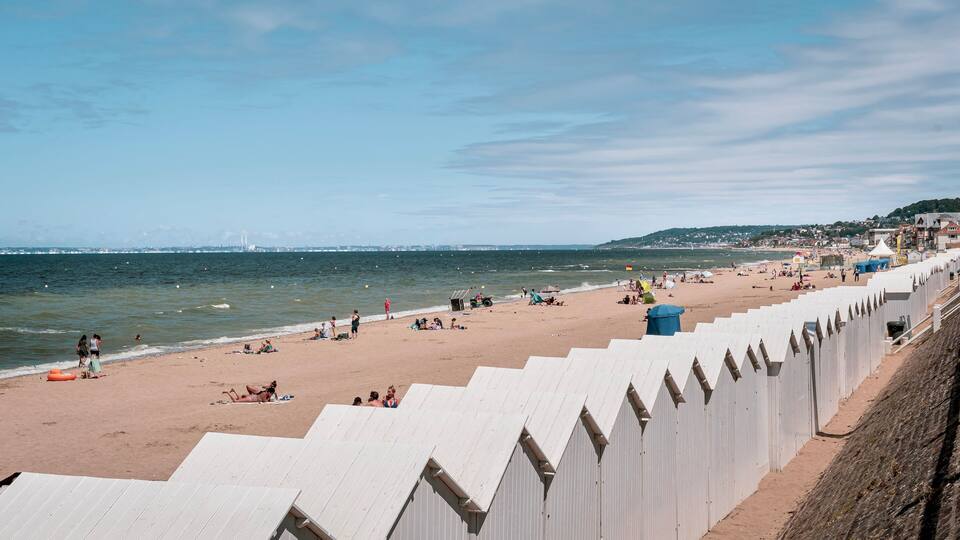 A beach with a wooden promenade, people sunbathing, and a distant cityscape.