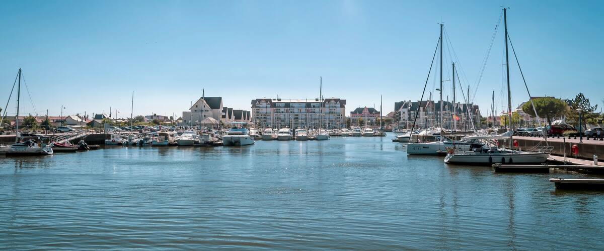A marina with numerous boats docked, a large building in the background, and a clear blue sky.