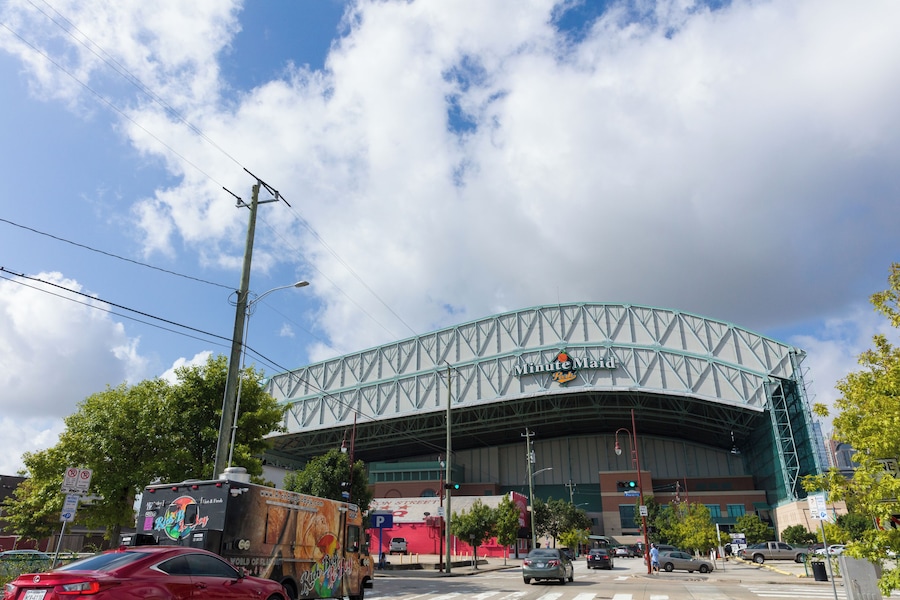 Street view of Minute Maid Park in downtown Houston, home of the Houston Astros, with cars and a food truck in front.