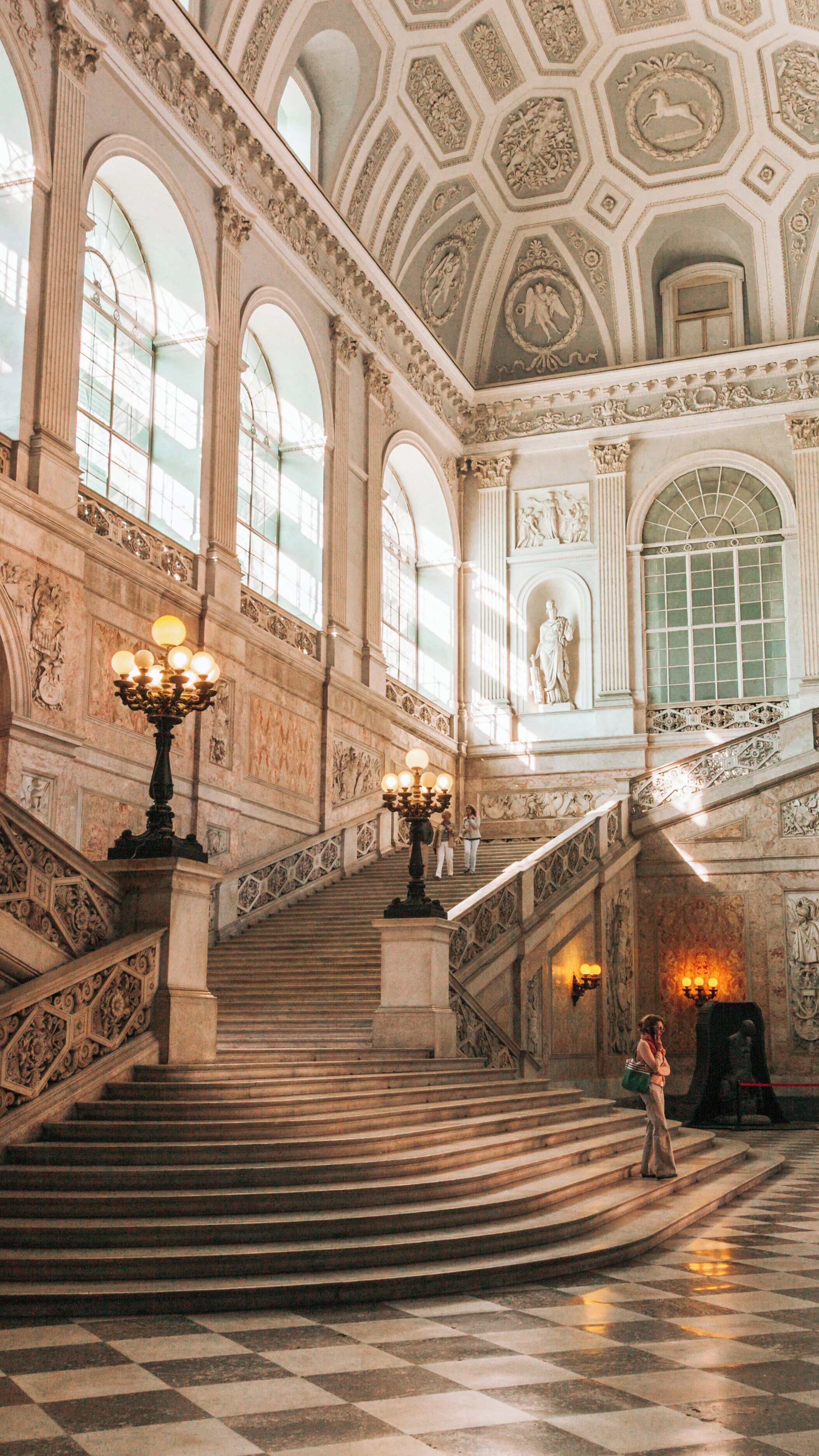 Majestic interior of Royal Palace in Chiaia, Naples showcasing grand staircase and intricate architectural details under soft sunlight