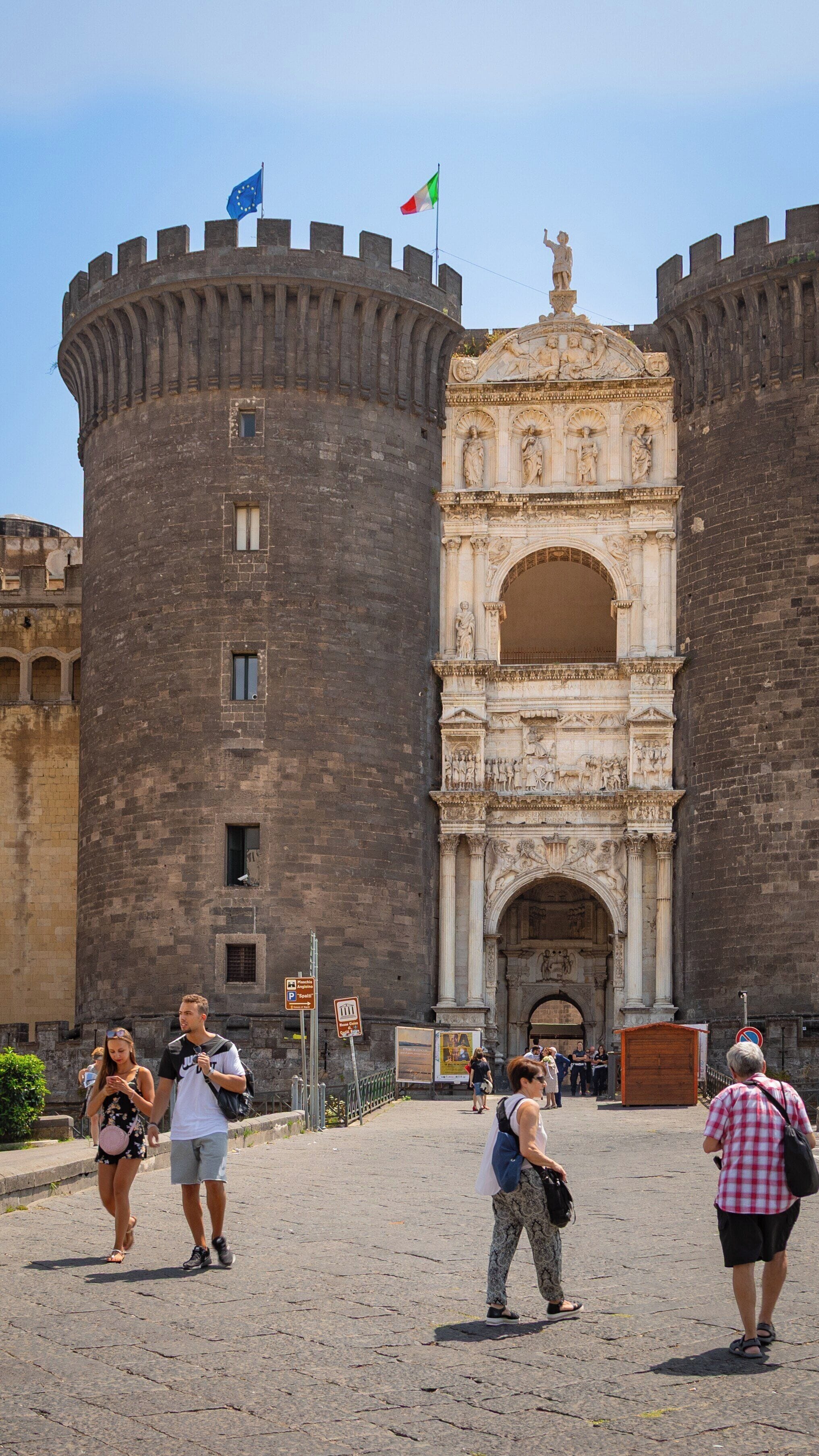 Visitors explore Castel Nuovo in Naples City Centre during a sunny day, admiring its historic architecture and vibrant atmosphere
