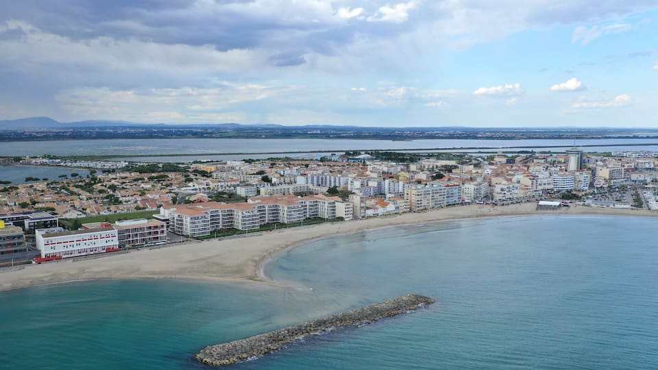 A coastal cityscape with a beach, buildings, and a distant mountain range.
