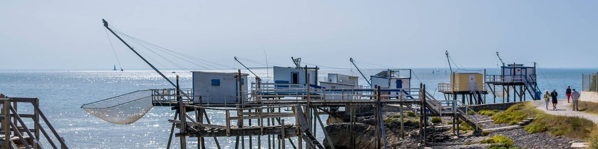 Un pueblo costero de pescadores con estructuras de madera sobre pilotes en el agua, cielo despejado y un camino a lo largo de la orilla.