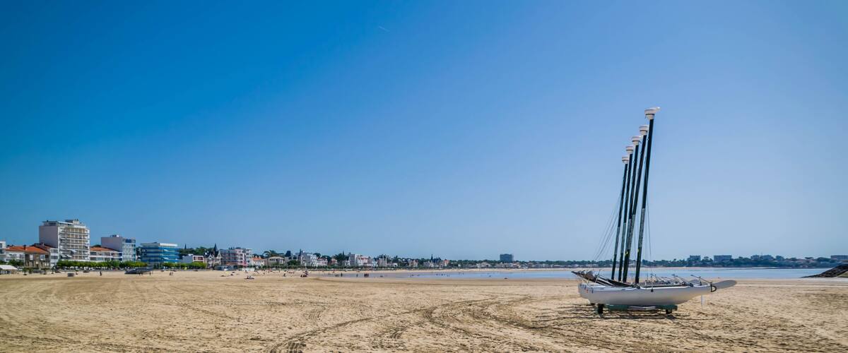 A sailboat on a sandy beach with buildings in the background.