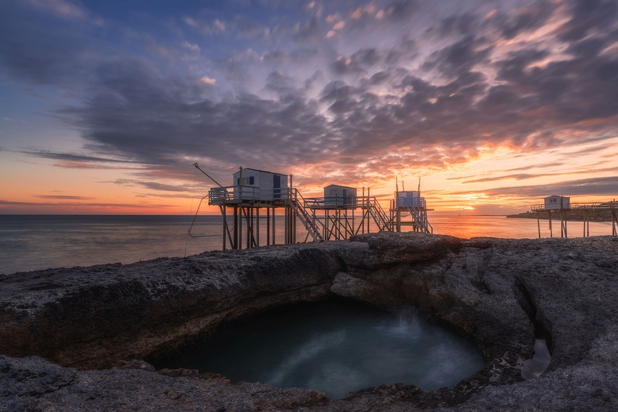Un tramonto su una costa rocciosa con un molo che si protende nell'acqua.