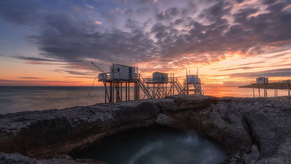 A sunset over a rocky coastline with a pier extending into the water.