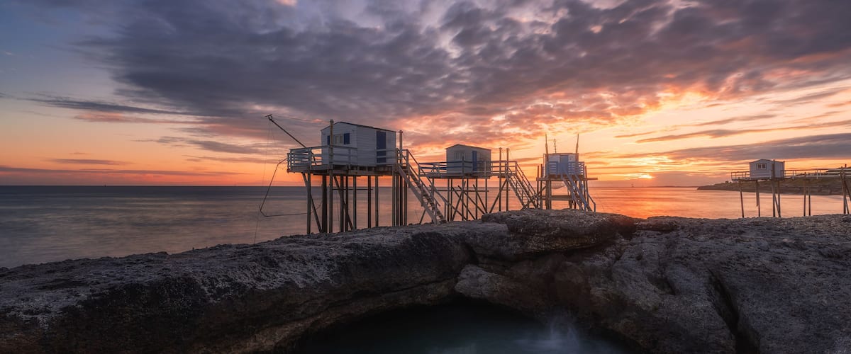 A sunset over a rocky coastline with a pier extending into the water.
