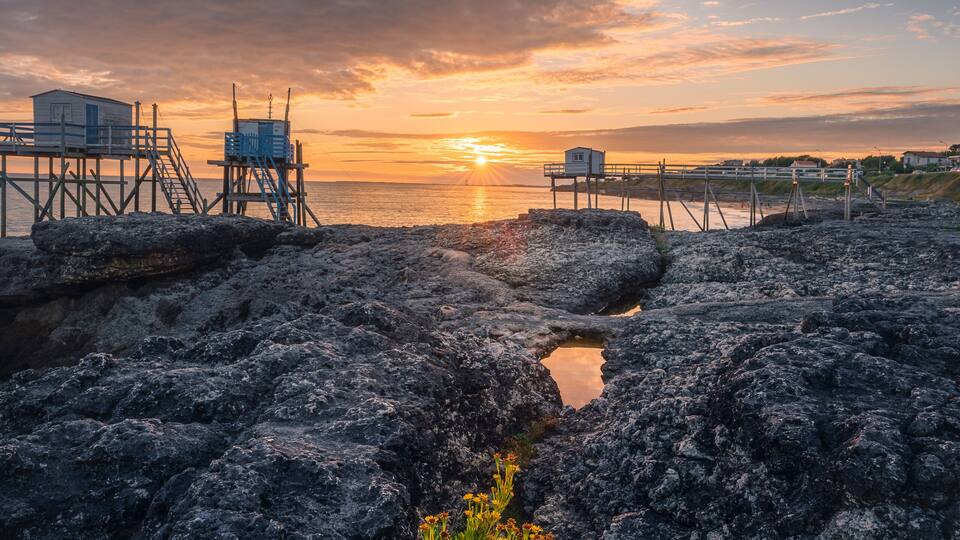 A rocky shoreline with a sunset, a lifeguard tower, and a small building.