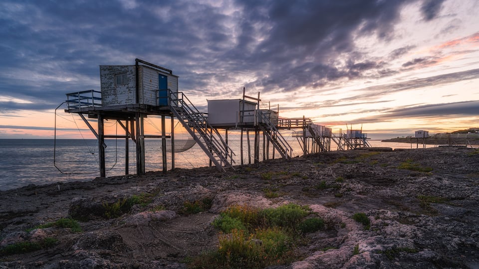 A coastal pier with a lifeguard station and a staircase leading to it, set against a sunset sky.