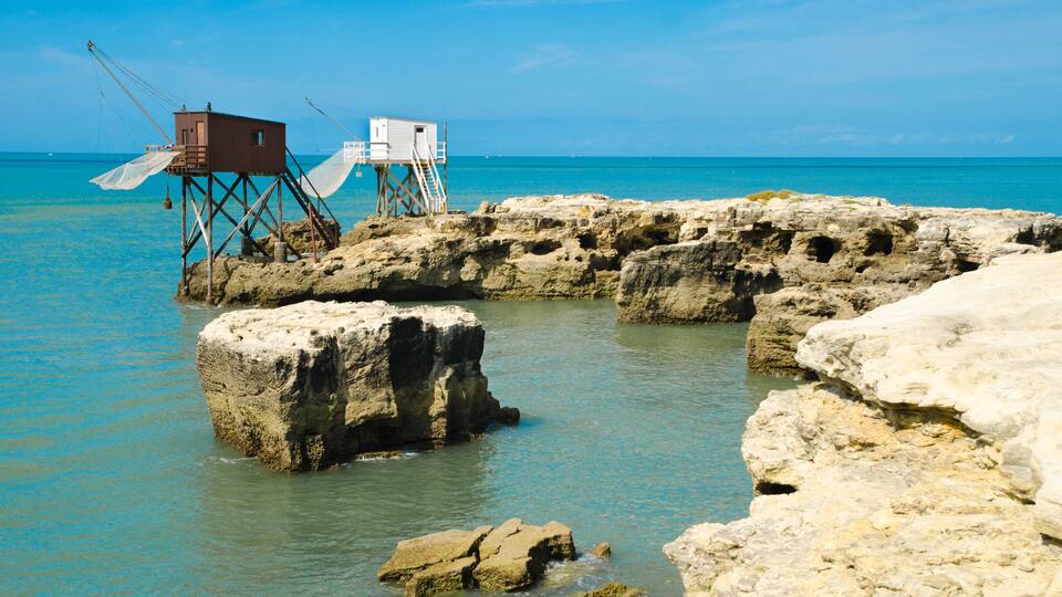 A rocky shoreline with fishing huts and a clear blue sea.