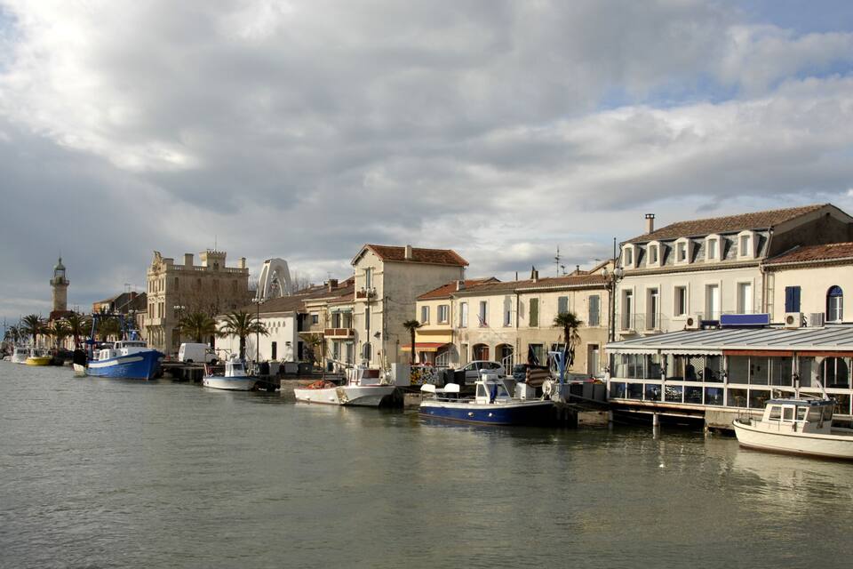 A harbor with boats docked along the waterfront, historic buildings, and a prominent tower in the background.