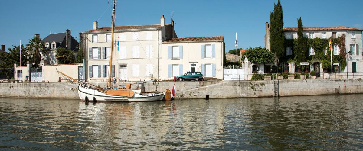 A calm river with a sailboat docked near a waterfront building.