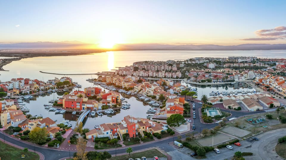 Eine Küstenstadt mit einem Jachthafen, Wohngebäuden und einem Sonnenuntergang über dem Wasser.