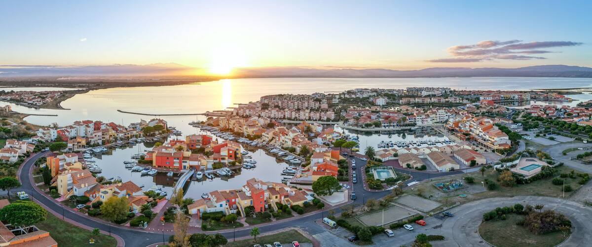 A coastal town with a marina, residential buildings, and a sunset over the water.