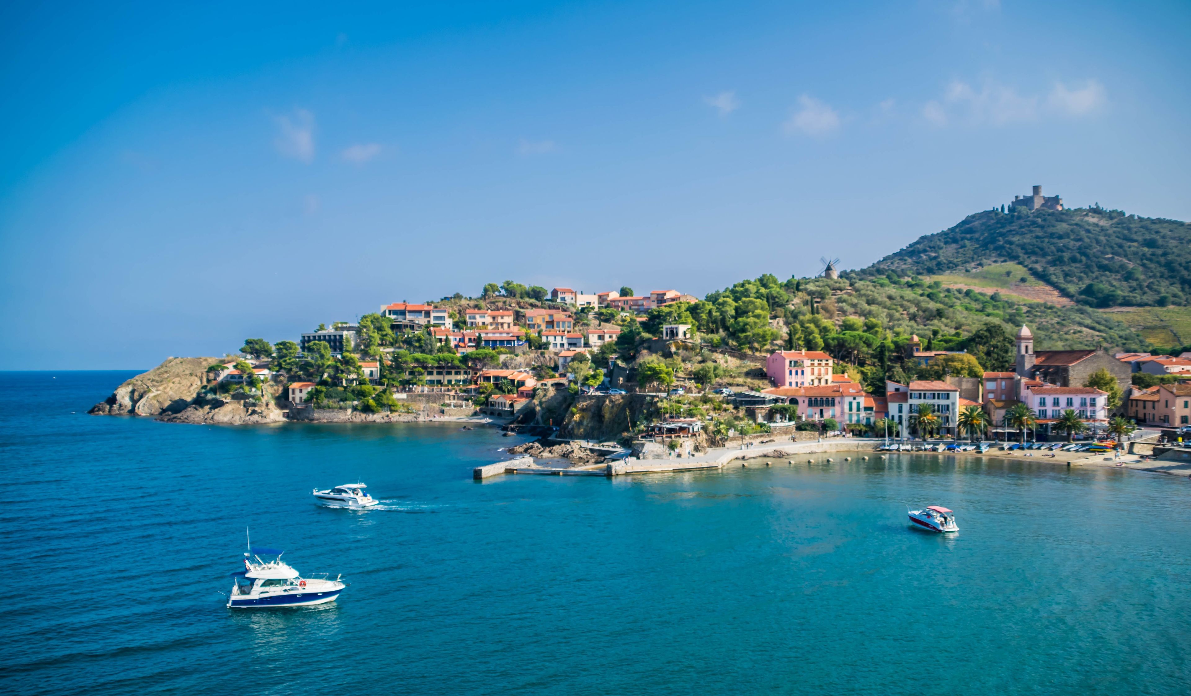 A coastal town with buildings on a hillside, boats on the water, and a windmill on the hill.