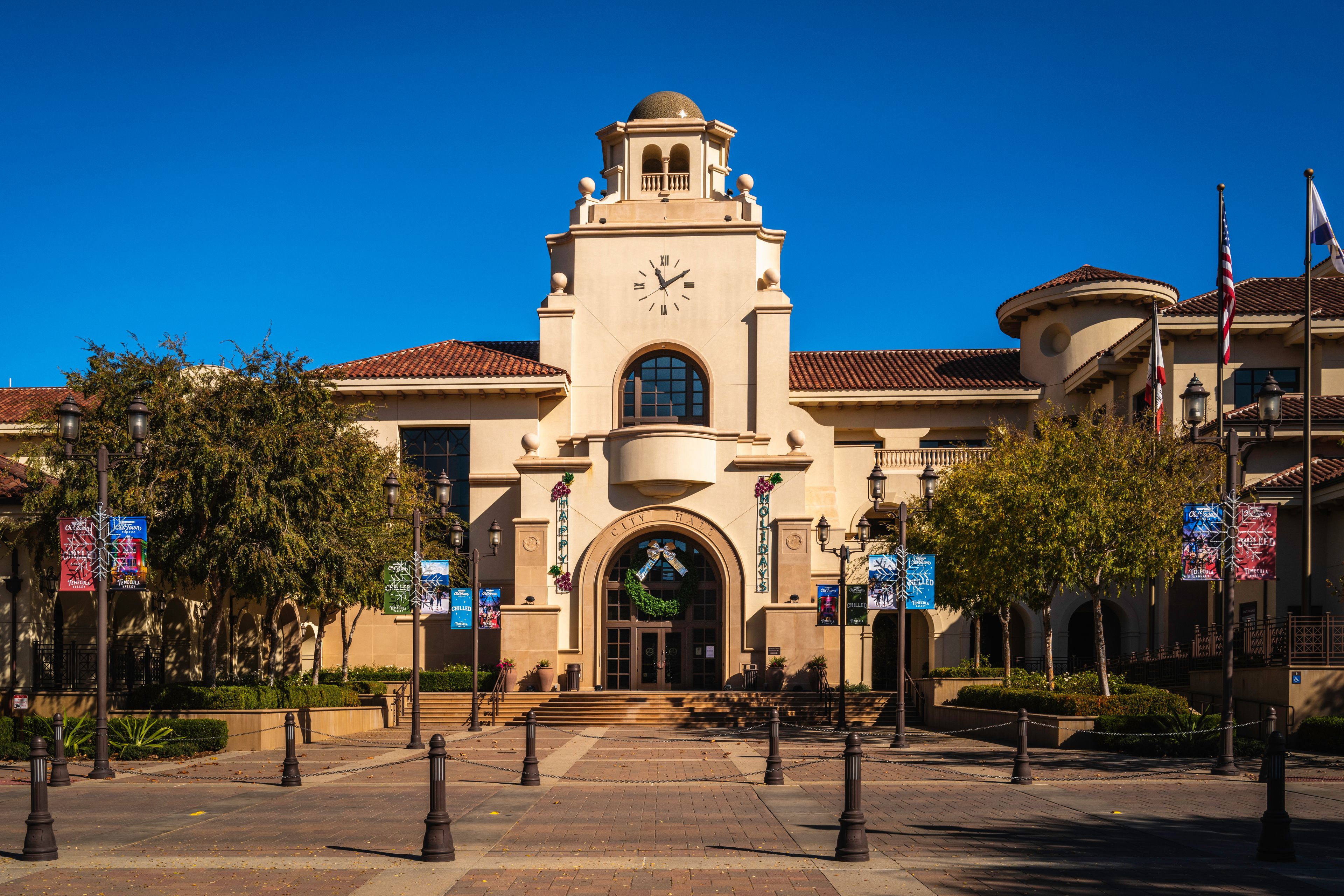 A historic building with a clock tower, arched entrance, and flags.