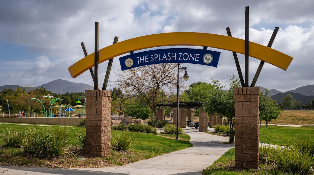 Winchester, CA, USA - April 11, 2022: Skinner Lake. Entrance bow over bow leading to Splash Zone, a kids playground with fountains under heavy blue cloudscape. Green garden setting.