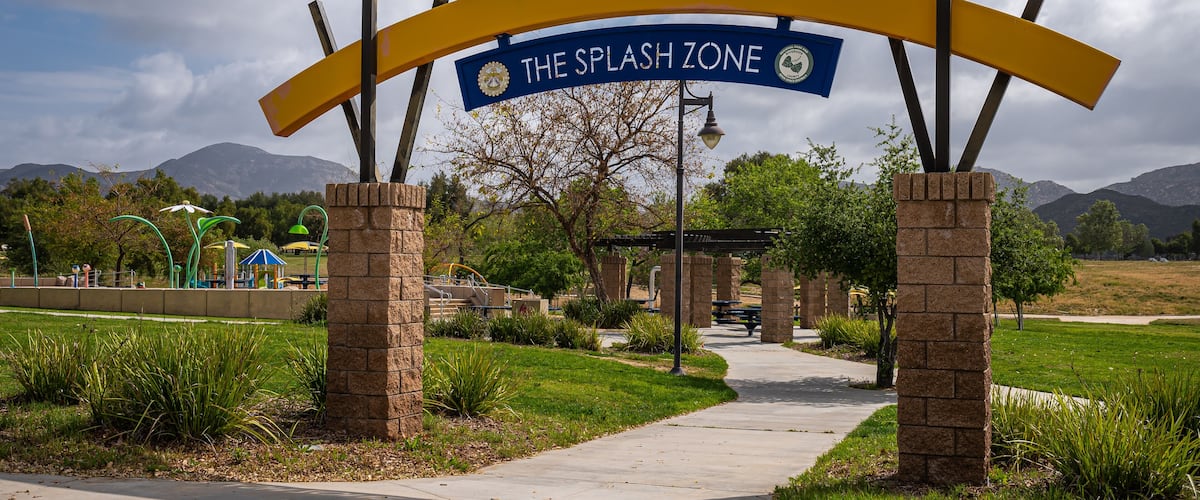 A park entrance with a sign reading 'The Splash Zone' and a pathway leading into the park.