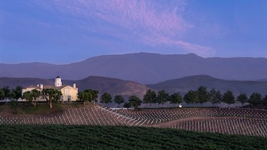 A church with a bell tower, a cemetery with headstones, and mountains in the background.
