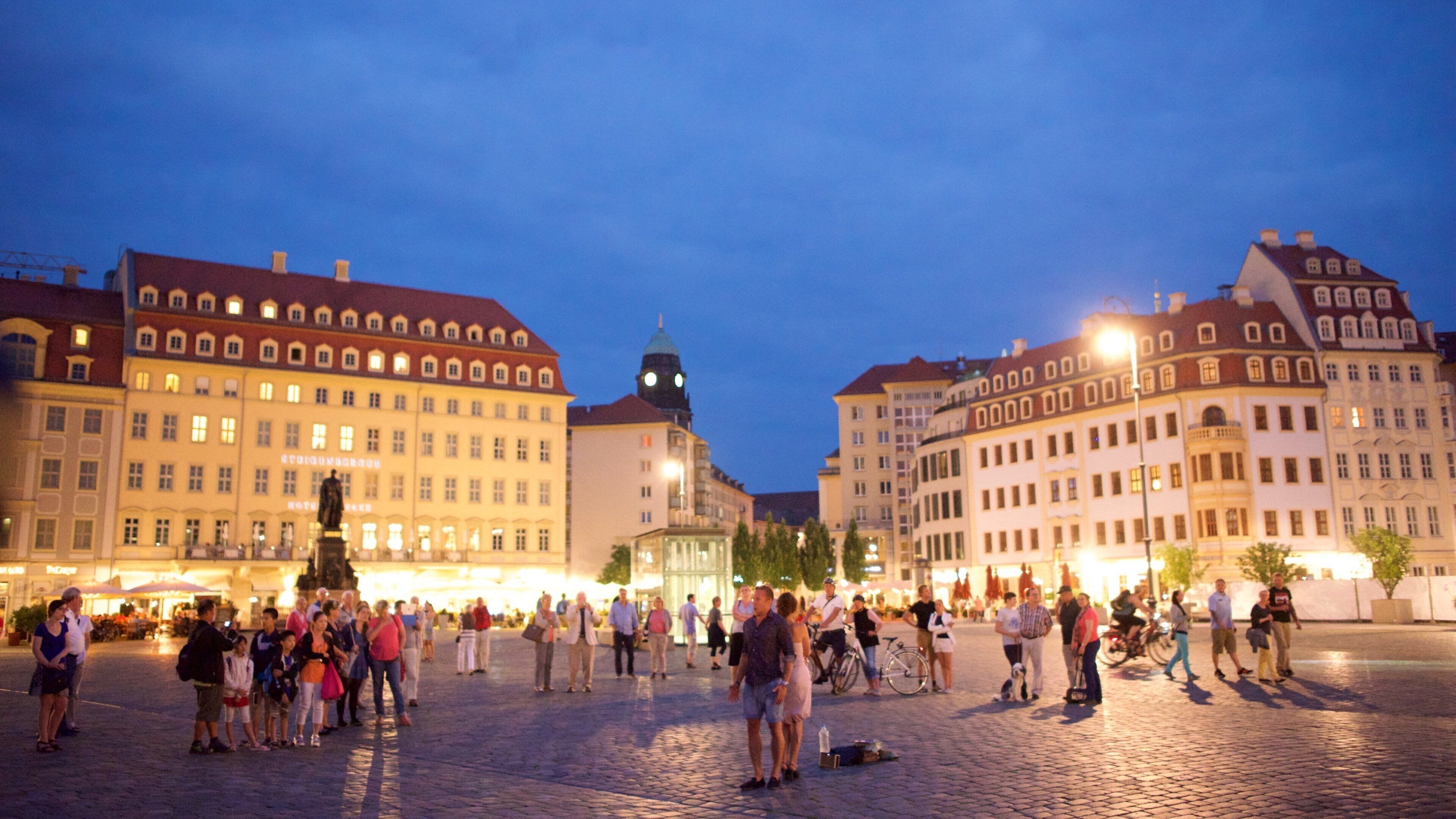 A historic square with cobblestone pavement, surrounded by classical European architecture and a prominent clock tower.