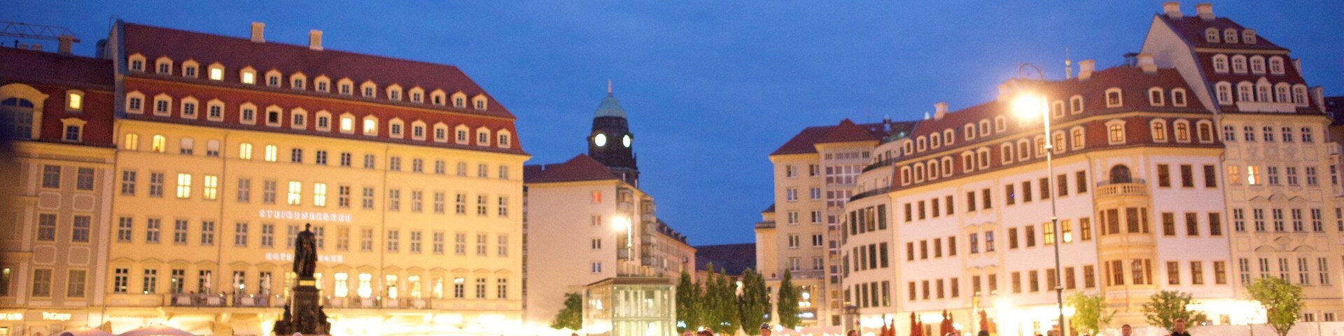 A historic square with cobblestone pavement, surrounded by classical European architecture and a prominent clock tower.