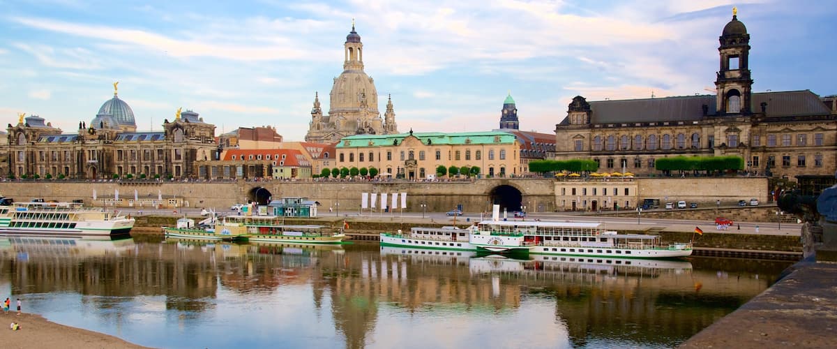 A river with boats, a sandy beach, and historic buildings in the background.