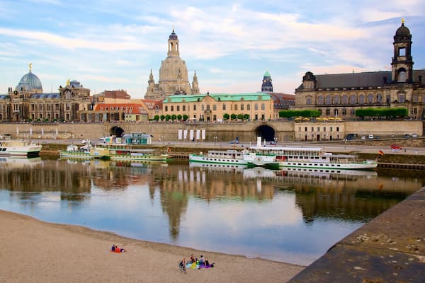 Ein Fluss mit Booten, ein Sandstrand und historische Gebäude im Hintergrund.