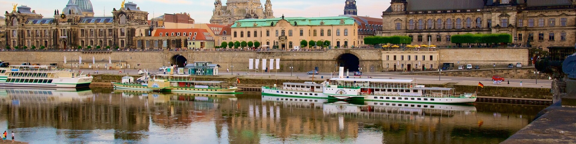 Un río con barcos, una playa de arena y edificios históricos al fondo.
