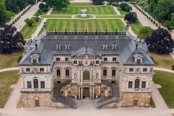 Ein prächtiges, historisches Gebäude mit symmetrischer Architektur, einer zentralen Treppe und einem formellen Garten mit einem Brunnen.
