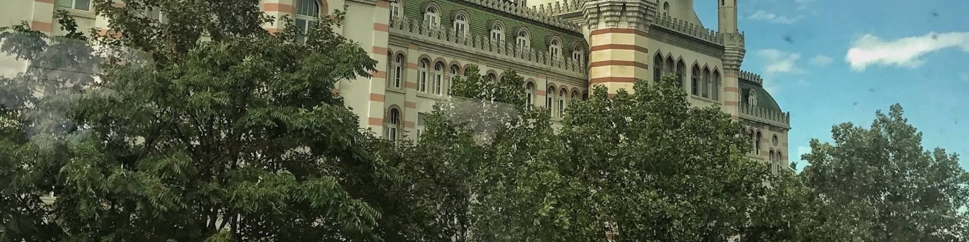 Un edificio histórico con una cúpula y agujas destacadas, rodeado de árboles.