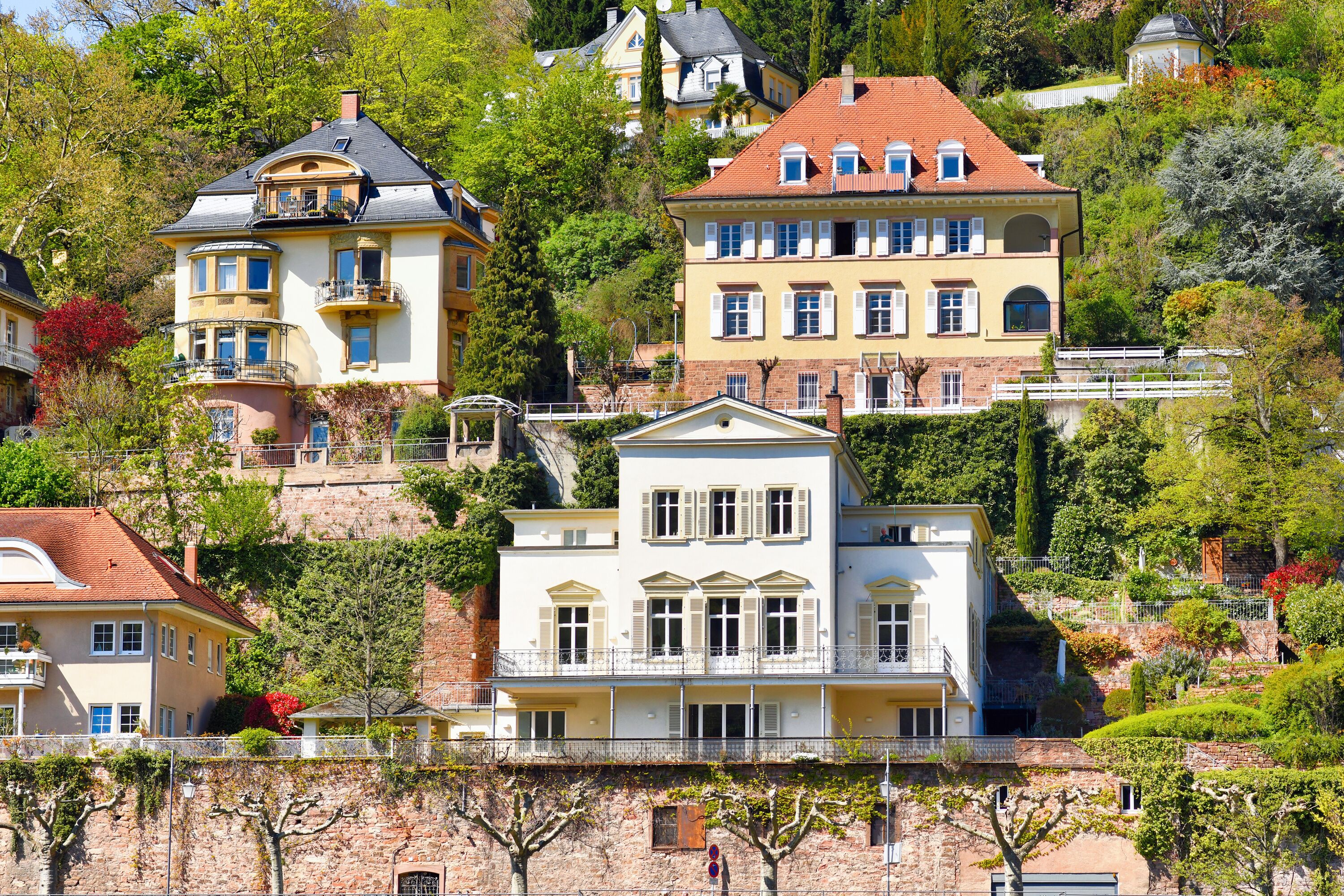A hillside with multi-story buildings, lush greenery, and a stone wall.
