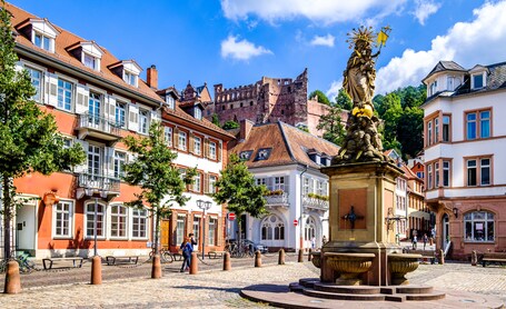 Ein historischer Platz mit einer Statue, Kopfsteinpflaster und traditioneller europäischer Architektur.