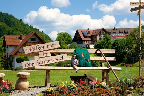 Une pancarte en bois sur laquelle on peut lire « Willkommen in Oberharmersbach » et un jeune garçon assis sur un banc.