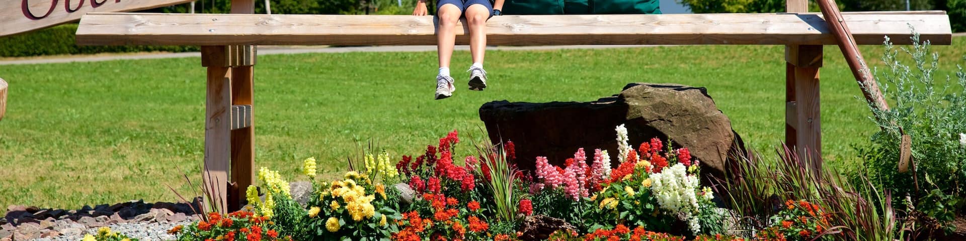 A wooden sign with "Willkommen in Oberhammersbach" and a child sitting on a bench.