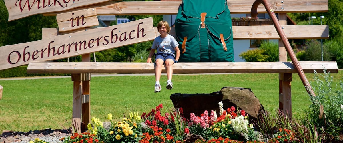 A wooden sign with "Willkommen in Oberhammersbach" and a child sitting on a bench.