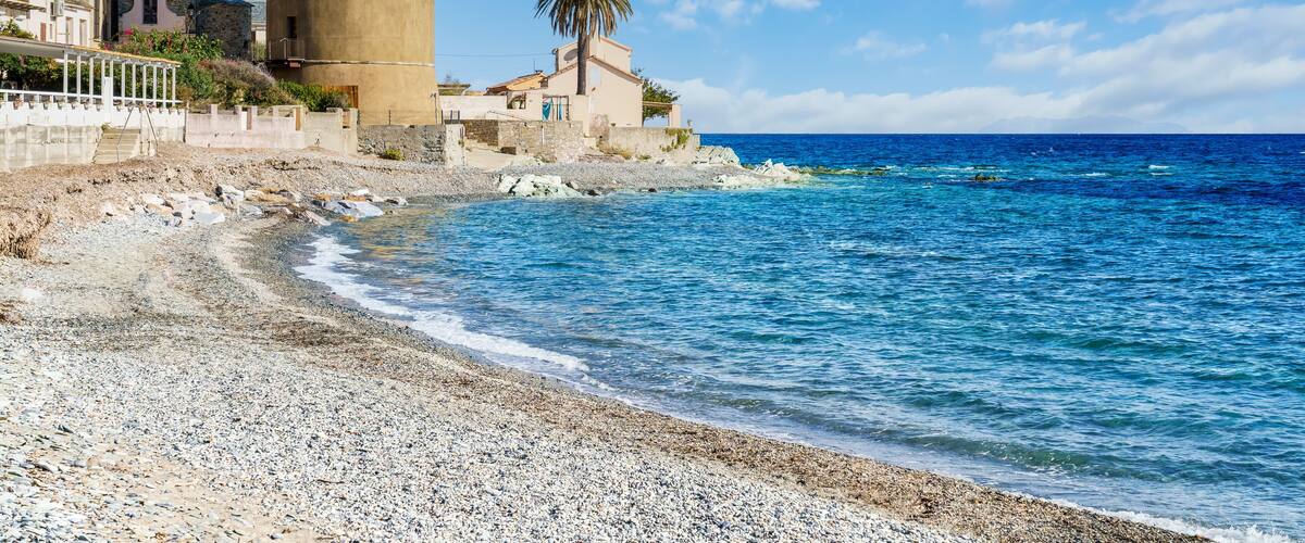A coastal town with a prominent tower, pebbly beach, and clear blue sea.